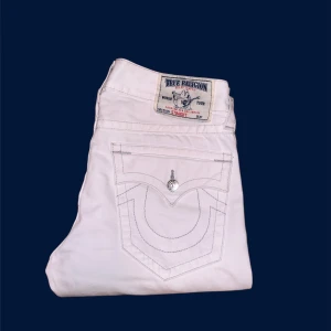 Vita jeansbyxor från True Religion - TAR ÄVEN BYTEN❗️Snygga vita jeansbyxor från True Religion med ikonisk broderad fickdesign. Byxorna har en klassisk femficksmodell och knappar i silverfärg. Perfekta för en stilren look.
