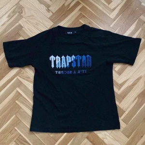 Svart t-shirt från Trapstar - Säljer en svart t-shirt från Trapstar med ett coolt tryck i blått och vitt på framsidan. T-shirten passar M/S och är kortärmad bara använd fåtal gånger