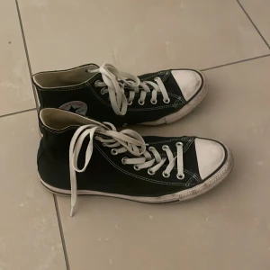 Svarta Converse All Star - Klassiska svarta Converse All Star med hög snörning och vit tåhätta. Skorna är i storlek 42 och är i bra skick.