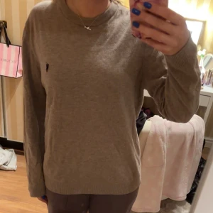 Beige tröja från Ralph Lauren - Säljer en stilren beige tröja från Ralph Lauren med långärmad design. Tröjan har en liten broderad logotyp på bröstet och är tillverkad i ett mjukt material. Perfekt för en avslappnad look.