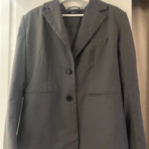 Grå kavaj från Gina Tricot - Snygg grå kavaj från Gina Tricot i storlek XS. Kavajen har en klassisk design med två knappar framtill och en stilren krage. 