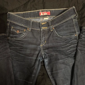 Mörkblå jeans från SoIn - Snygga mörkblå jeans från SoIn med kontrastsömmar och klassisk femficksdesign. Jeansen har en knappgylf och dekorativa sömmar på bakfickorna. Perfekta för en stilren look.