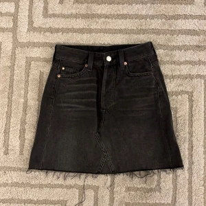 Svart jeanskjol  - Snygg svart jeanskjol från H&M med klassisk femficksdesign. Kjolen har en knapp och dragkedja framtill samt två bakfickor. 100% bomull, mycket bra skick och storlek xs