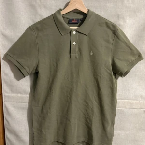 Olivgrön pikétröja från Morris - Snygg olivgrön pikétröja från Morris med klassisk krage och två knappar. Tröjan har korta ärmar och en diskret broderad logga på bröstet. Perfekt för en stilren look.