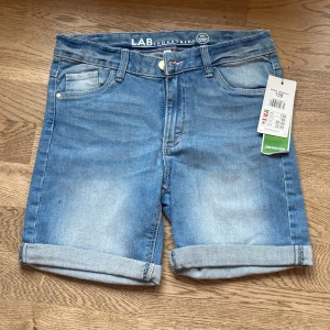 Blå jeansshorts från LAB Industries - Snygga blå jeansshorts från LAB Industries i en klassisk design. De har en normal passform med upprullade benslut och femficksmodell. Perfekta för en avslappnad stil med en touch av hållbarhet.