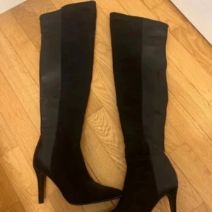 Svarta höga stövlar med klack - Snygga svarta stövlar i mocka med hög klack och spetsig tå. Perfekta för en elegant look. De har en dragkedja på insidan för enkel på- och avtagning.