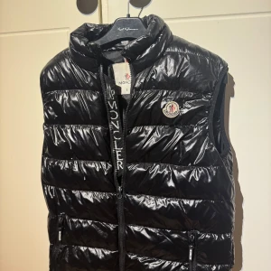 Moncler dunväst - Säljer en svart dunväst från Moncler i storlek S och är i helt okej skick och är ganska smutsig på bild men annars så är den i bra skick.