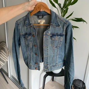 Blå jeansjacka från A Jacket - Säljer en snygg blå jeansjacka från A Jacket. Jackan är croppad med knappar framtill och har två bröstfickor med knappstängning. Perfekt för en avslappnad stil!