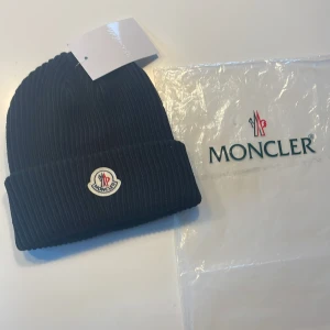 Svart ribbad mössa från Moncler - Snygg svart ribbad mössa från Moncler med broderad logotyp framtill. Perfekt för kyliga dagar och ger en stilren look. Priset kan diskuteras