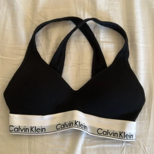 Svart sporttopp från Calvin Klein - Snygg svart sporttopp från Calvin Klein med korsade axelband och elastiskt band med logotyp. Perfekt för träning eller en avslappnad look. Är helt ny och är köpt för 400kr