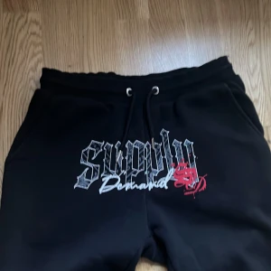Svarta mjukisbyxor med tryck - Snygga svarta mjukisbyxor med coolt tryck framtill. Byxorna har en bekväm passform med snörning i midjan för justerbarhet. Perfekta för en avslappnad stil.