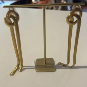 Guldörhängen med knutdesign - Eleganta guldörhängen med unik knutdesign. De långa hängen ger en stilren och modern look. Perfekta för att ge en extra touch till din outfit.