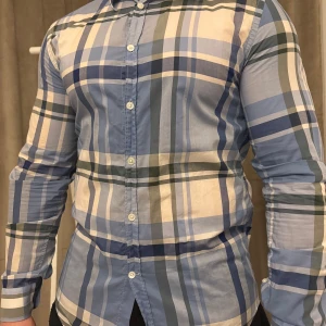 Rutig skjorta från Acne - Snygg rutig skjorta från Acne i blå, grön och vit. Skjortan har långa ärmar och knappar framtill. Perfekt för en stilren look.