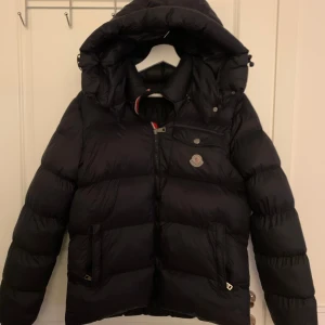 Svart dunjacka från Moncler - Säljer en snygg svart dunjacka från Moncler. Jackan har en quiltad design med en dragkedja framtill och en praktisk huva. Perfekt för kyliga dagar och håller dig varm och stilren. Och har en liten reva som är lagad med lim på ärmem. Kartonen finns skriv till mig så skickar jag bild på den. Pris kan diskuteras!🖤