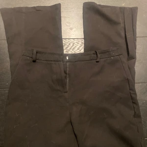 Svarta kostymbyxor - Snygga svarta kostymbyxor med en klassisk design. De har en rak passform och är perfekta för en stilren look. Byxorna har hällor för bälte och en diskret dragkedja framtill.