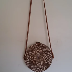 Rund flätad axelväska - Flätad axelväska i brunt och beige. Aldrig använt, locket på väskan är lite vingligt när den är öppen annars är den bra!!