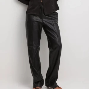 Svarta skinnbyxor - Snygga svarta skinnbyxor med hög midja och rak passform. Byxorna har en stilren design med diskreta fickor och bälteshällor. Perfekta för en trendig look.