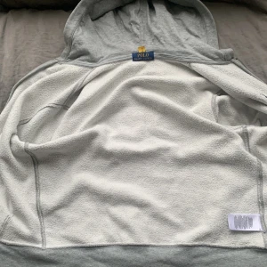 Grå hoodie från Polo Ralph Lauren - Säljer en grå hoodie från Polo Ralph Lauren med dragkedja och kängurufickor. Den har en broderad logga på bröstet och är tillverkad i mjukt material för extra komfort. Perfekt för en avslappnad stil. Är för liten för mig. Pris kan diskuteras 