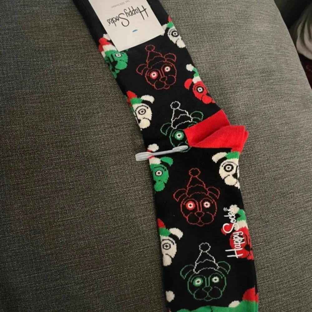 Ett par färgglada jul strumpor från Happy Socks med ett lekfullt mönster av hundansikten i rött, grönt och vitt på svart bakgrund. Har flera par - annonsen gäller 1 par. Muu.