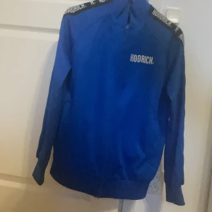  Hoodrich - Snygg blå tröja från Hoodrich med dragkedja och textdetaljer på axlarna. Perfekt för en sportig look med långärmade ärmar och ribbade muddar.