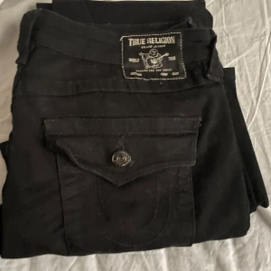 True religon low waist - Snygga svarta jeans från True Religion med klassisk femficksdesign och knappdetaljer. Perfekta för en stilren look. Passar bra till både vardag och mer uppklädda tillfällen. Köptes för 1500kr från nelly säljer pga ingen användning, säljer för 1000kr!