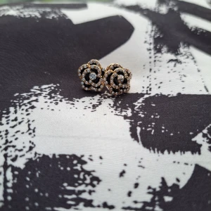 Guldiga örhängen med blommönster - Snygga guldiga örhängen i form av blommor med glittriga detaljer. Perfekta för att ge en elegant touch till din outfit. Passar både till vardag och fest. Guldpläterade, typ 1cm stora.