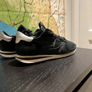 Philippe Model Trainers - Snygga svarta sneakers från Philippe Model med vita detaljer. Skorna har en klassisk design med snörning och en bekväm sula. Perfekta för en stilren look. De är perfekta nu inför vintern! Riktigt snygga skor! Ord pris: 3500 kr. Mitt pris 1600kr! Skorna är i storlek 39 men passar även 40! Hör av er vid andra funderingar!🤝💯💥