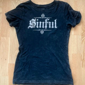 Rhinestone sinful/affliction t-shirt - Säljer coola  sinful/affliction svart t-shirt med tryck i vitt på framsidan och stora vingmotiv på baksidan. Säljer den eftersom den inte kommer till användning, använd bara två gånger. Pris kan diskuteras 
