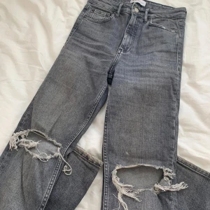 Grå jeans med slitningar från Zara - Snygga grå jeans från Zara med coola slitningar på knäna. De har en klassisk femficksdesign och en knappgylf. Perfekta för en avslappnad look med en touch av edge.