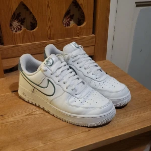 Nike Air Force 1 '07 LV8 i vitt och mint detaljer - Snygga Nike Air Force 1 '07 LV8 sneakers i vitt med gröna detaljer. Klassisk design med snörning och perforerad tå för ventilation. Perfekta för en stilren look.