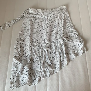 Vit prickig kjol - Säljer denna vita kjol med svarta prickar och snöre på sidan då den inte kommer till användning längre. Nästan helt ny och oanvänd. Ny skick. Skriv privat vid frågor.