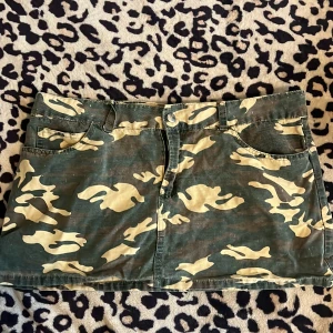Camouflage kjol från Rich Jeans - Snygg kortkjol i camouflage från Rich Jeans. Kjolen har en klassisk femficksdesign och stängs med dragkedja och knapp framtill. Perfekt för en cool och avslappnad stil.