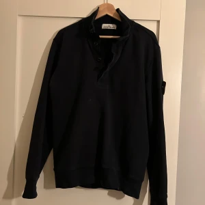 Marinblå tröja från Stone Island - Säljer en stilren svart tröja från Stone Island med knappar vid halsen och även dragkedja. Patch på armen och sjävklart äkta!