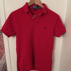 Röd pikétröja från Ralph Lauren - Säljer en klassisk röd pikétröja från Ralph Lauren. Perfekt för en stilren och avslappnad look. Tröjan har en normal passform och är tillverkad i ett bekvämt material. Passar året runt