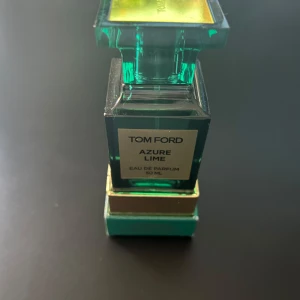 Tom Ford Azure Lime Eau de Parfum - Elegant flaska med en fräsch doft av Azure Lime från Tom Ford. Flaskan är i en stilren, fyrkantig design med en turkos nyans och gulddetaljer. Perfekt för den som älskar en uppfriskande och lyxig doftupplevelse.