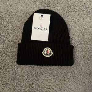 Svart ribbad mössa från Moncler - Snygg svart ribbad mössa från Moncler med broderad logotyp framtill. Perfekt för att hålla värmen under kyliga dagar. Stilren design som passar till det mesta.