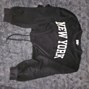 Svart sweatshirt från Only - Säljer en svart sweatshirt från Only med texten 'New York' i vitt på framsidan. Tröjan har långa ärmar och en justerbar dragsko i nederkanten. Perfekt för en avslappnad stil.