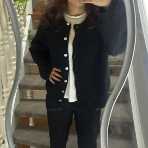 Svart kofta från Gina Tricot - Säljer en stilren svart kofta från Gina Tricot i premiumkvalitet. Koftan har långa ärmar och knäpps med knappar framtill. 