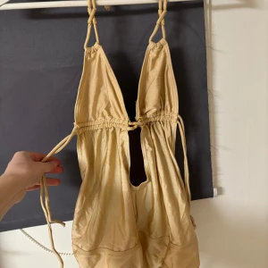 Guld baddräkt från By Malene Birger - Snygg guld baddräkt med knytband och djup urringning från By Malene Birger. Tillverkad i en mjuk och stretchig polyamidblandning som ger en bekväm passform. Perfekt för en dag på stranden eller vid poolen.