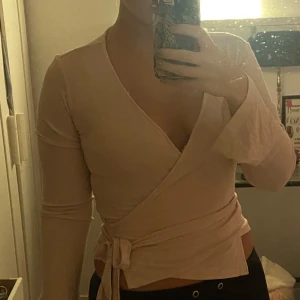 Rosa omlottopp från Gina Tricot - Säljer en ljust rosa omlottopp från Gina Tricot. Toppen har långa ärmar och ett knytband i midjan. Enbart använd en gång då den inte är min stil.