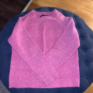 Rosa stickad tröja från Vero Moda - Mysig rosa stickad tröja från Vero Moda. Perfekt för kyliga dagar med sin mjuka och bekväma passform. Tröjan har långa ärmar och en enkel design som gör den lätt att matcha med olika outfits.