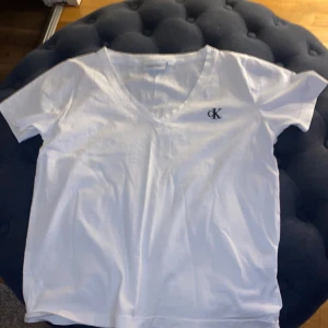 Vit t-shirt från Calvin Klein - Säljer en stilren vit t-shirt från Calvin Klein med v-ringning och korta ärmar. Den har en diskret CK-logga broderad på bröstet. Sitter som i xs så blir inte stretchig eller så.