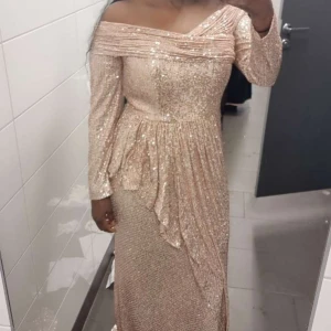 Champagnefärgad glittrig långklänning - Köpt från REMANNS för 3400kr, bröllopsbutik i Göteborg. Använd en gång endast! Det  Elegant champagnefärgad långklänning med glittrande paljetter. Klänningen har en offshoulder-design och långa ärmar, vilket ger en sofistikerad look. Perfekt för festliga tillfällen. 