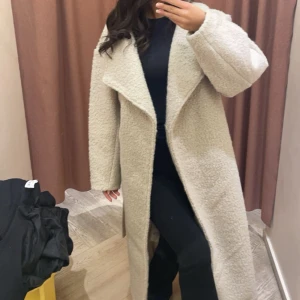 Beige teddyjacka med bälte - Säljer en mysig beige teddyjacka med bälte. Jackan har en lång och avslappnad passform med breda slag och långa ärmar. Perfekt för kyliga dagar när du vill hålla dig varm och stilren.