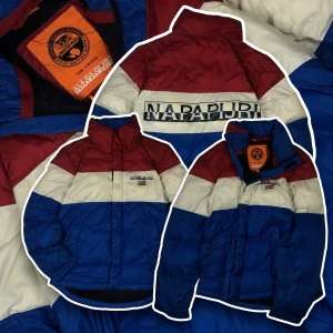 Flerfärgad dunjacka från Napapijri - Säljer en snygg flerfärgad dunjacka från Napapijri i rött, vitt och blått. Jackan har en hög krage och dragkedja framtill. Perfekt för kyliga dagar med sin quiltade design och varma material. Chest 44cm. , sleeve length 60 cm. , length form shoulder 66cm.