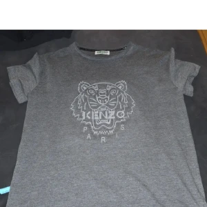 Grå t-shirt från Kenzo - Snygg grå t-shirt från Kenzo med ett stort tigertryck och texten 'Kenzo Paris' på framsidan. Perfekt för en casual look.