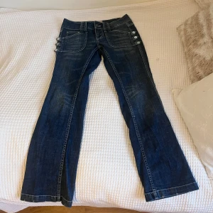 Mörkblå bootcut låg/mid rise jeans - Snygga mörkblå jeans från b.young med unika knapprader på sidorna. De har en bootcut-stil och är i bra skick. Jeansen har as snygga fickor! Midjemått: 37 cm rakt över. Innerben: 76 cm. De är aningen för korta i stilen för mig som är 168 cm! Skriv om du vill ha bild på eller har andra frågor 😋! 