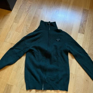 Svart tröja med dragkedja från GANT - Snygg svart tröja från GANT med dragkedja och broderad logga på bröstet. Skick 8/10 ursprungligen Mediym, men passar numera storlek S, har blivit mindre i tvätten