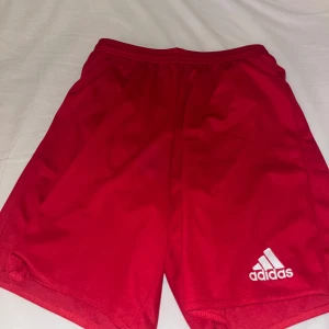 Röda träningsshorts från Adidas - Snygga röda träningsshorts från Adidas med Climalite-teknologi för optimal komfort. Perfekta för sport och träning. Elastisk midja för en bekväm passform.