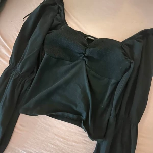 Svart offshoulder topp från BikBok - Snygg svart offshoulder topp från BikBok i storlek XS. Toppen har en smockad byst och långa ärmar med en lätt volangdetalj vid axlarna. Perfekt för en stilren look.